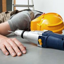 A person laying on the ground with a drill and hard hat