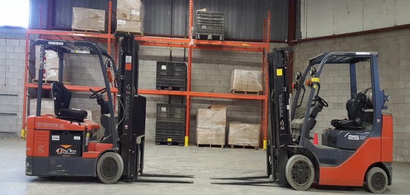 Two fork lifts in a warehouse with boxes on the shelves.