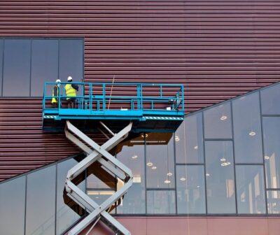 Two men in a scissor lift next to a building.