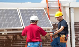 Two men in hard hats and safety glasses working on a solar panel.