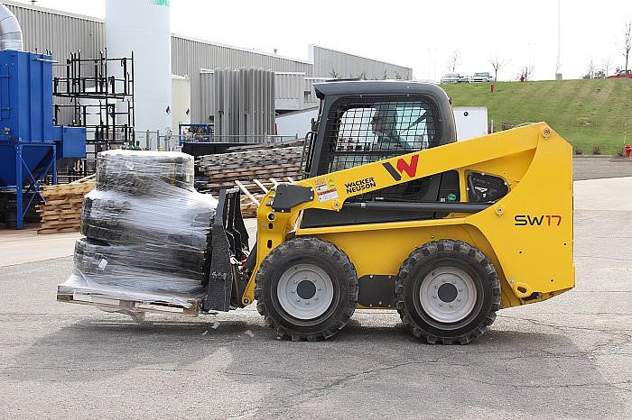 A yellow and black skid steer is pulling a pallet.
